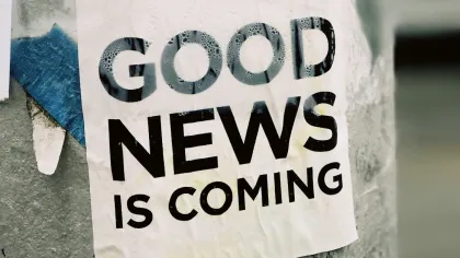 Poster with bold text 'GOOD NEWS IS COMING' attached to a weathered pole in an urban environment.