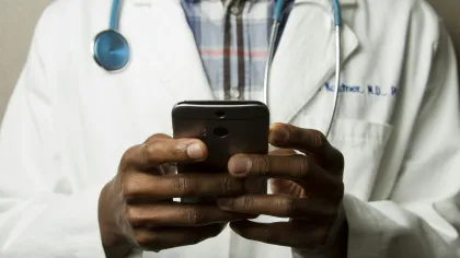 A doctor in a white coat uses a smartphone, highlighting modern healthcare and technology integration.