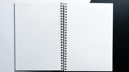 Open blank spiral notebook lying flat on contrasting black and white surface, ready for writing or drawing.