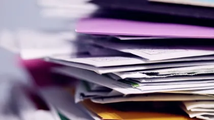 Close-up of a thick pile of assorted colorful papers, envelopes, and documents stacked on a white surface.