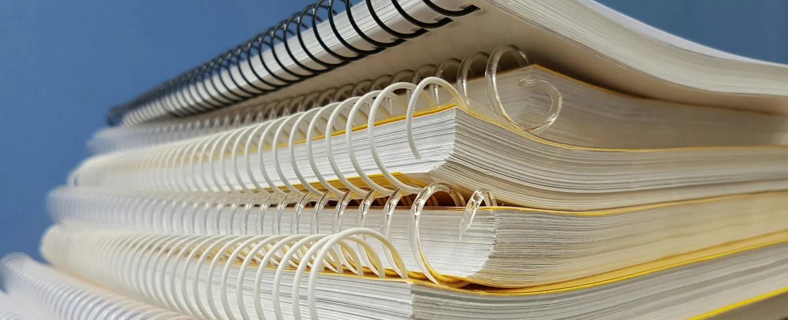Stack of spiral-bound notebooks in various colors against a blue background.