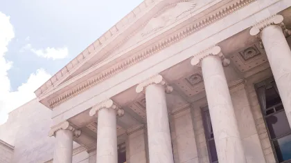 Close-up of grand marble columns and pediment of a historic courthouse building under a bright sky.