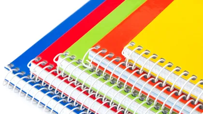 Stack of colorful spiral notebooks with yellow, orange, green, red, and blue covers on white background